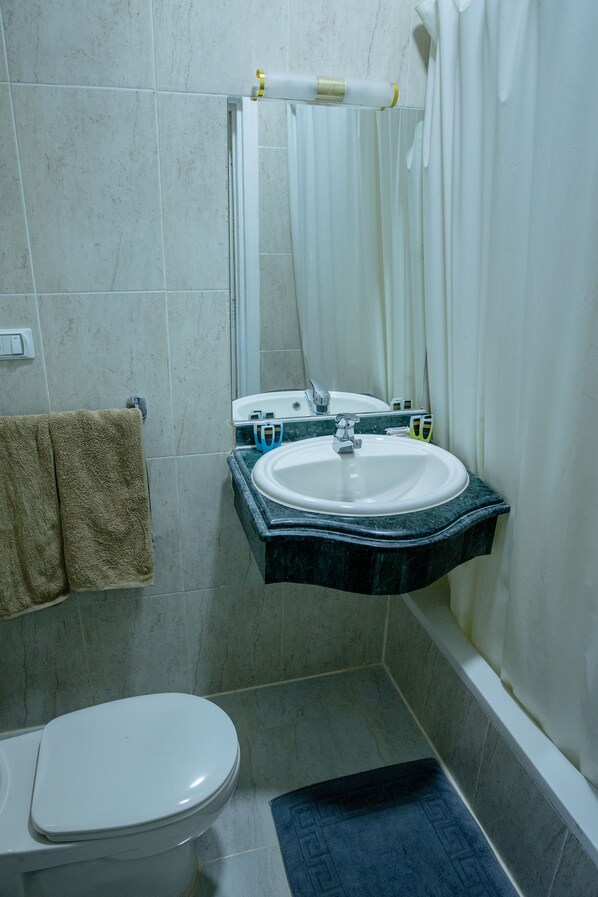 Un baño con inodoro blanco, lavamanos con espejo y cortina de ducha.