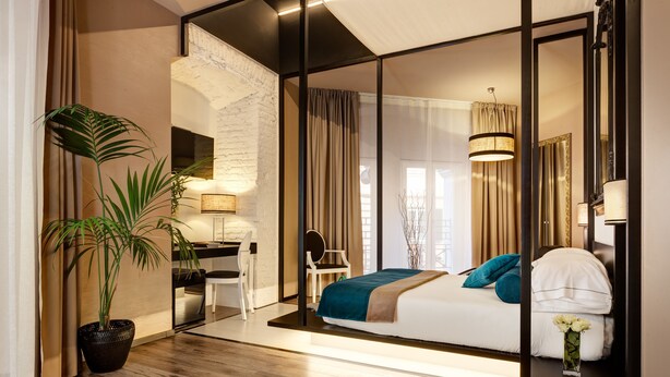 A modern hotel room with a bed, a desk, a chair, a potted plant, and a large mirror. -  Dharma Luxury Hotel & Spa. (Rome)