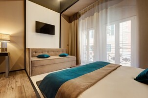 Una moderna camera d'hotel con un letto, una poltrona, una TV a parete e un balcone con tende.