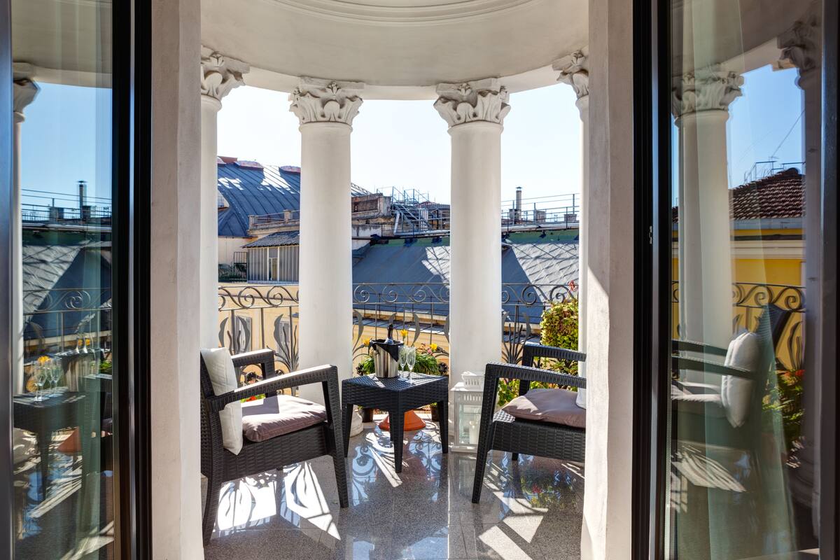 A balcony with two wicker chairs, a small table, and a glass railing.
