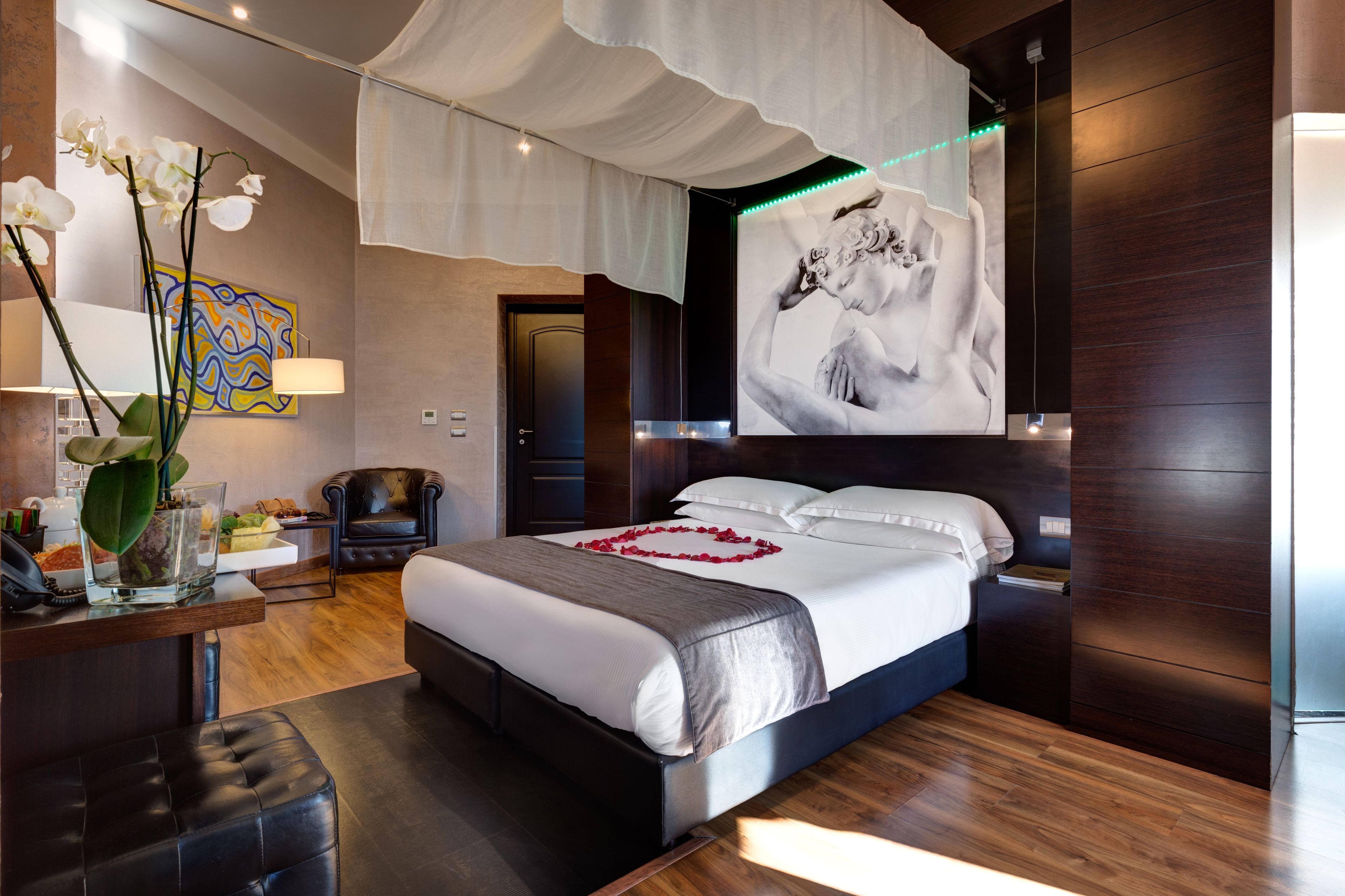 Una camera d'albergo moderna con un letto grande, una scrivania con una lampada, un vaso con fiori e un quadro appeso al muro.