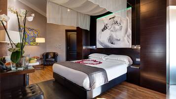 Una camera d'albergo moderna con un letto grande, una scrivania con una lampada, un vaso con fiori e un quadro appeso al muro.