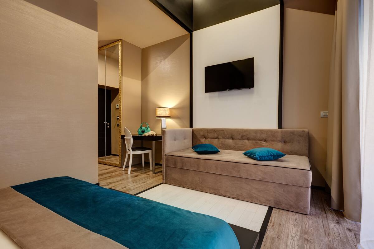 A hotel room with a sofa, a bed, a TV mounted on the wall, and a desk with a chair.