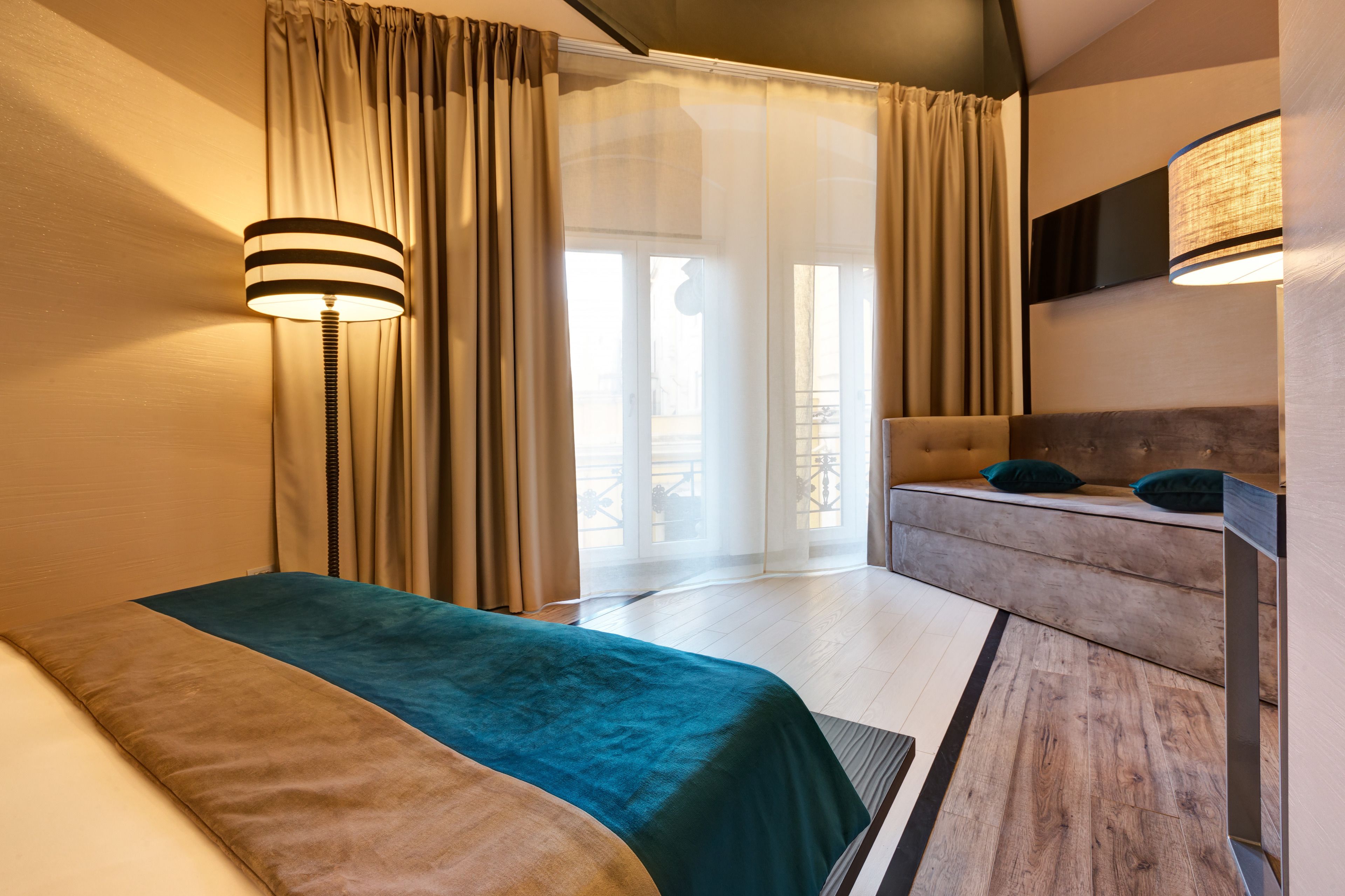 Una camera d'albergo con un letto, un divano, una lampada e vista sull'esterno.