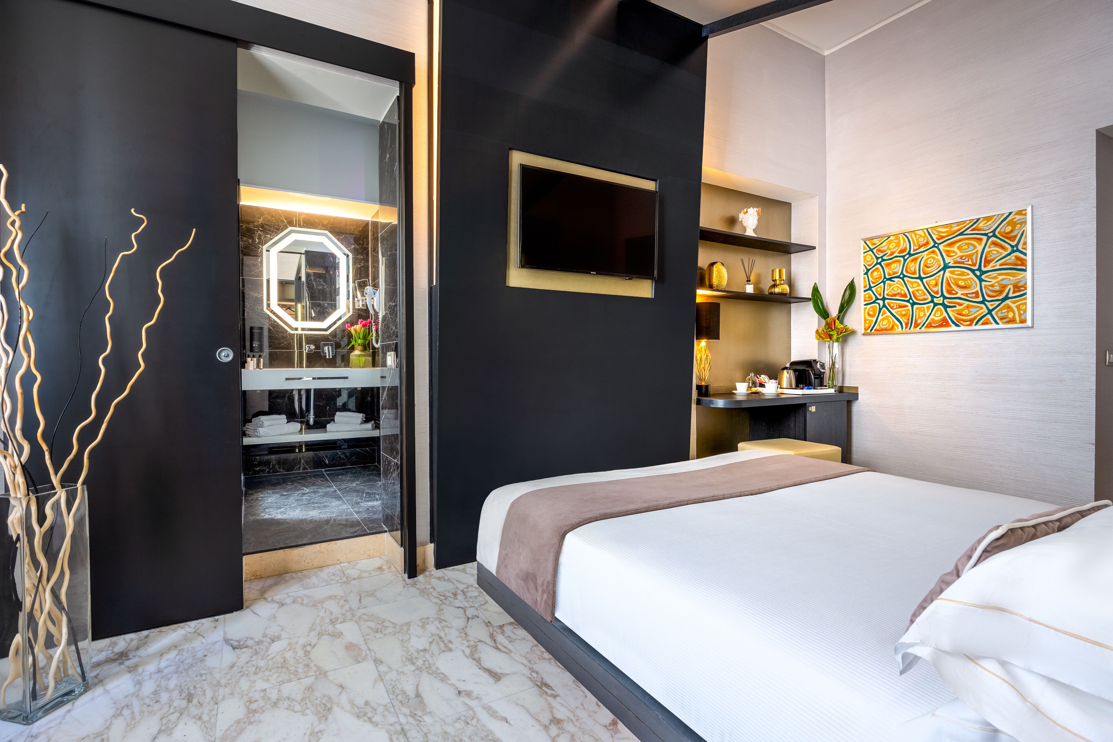 Camera d'albergo moderna con un grande letto, televisione, uno specchio e bagno visibile attraverso una porta aperta.