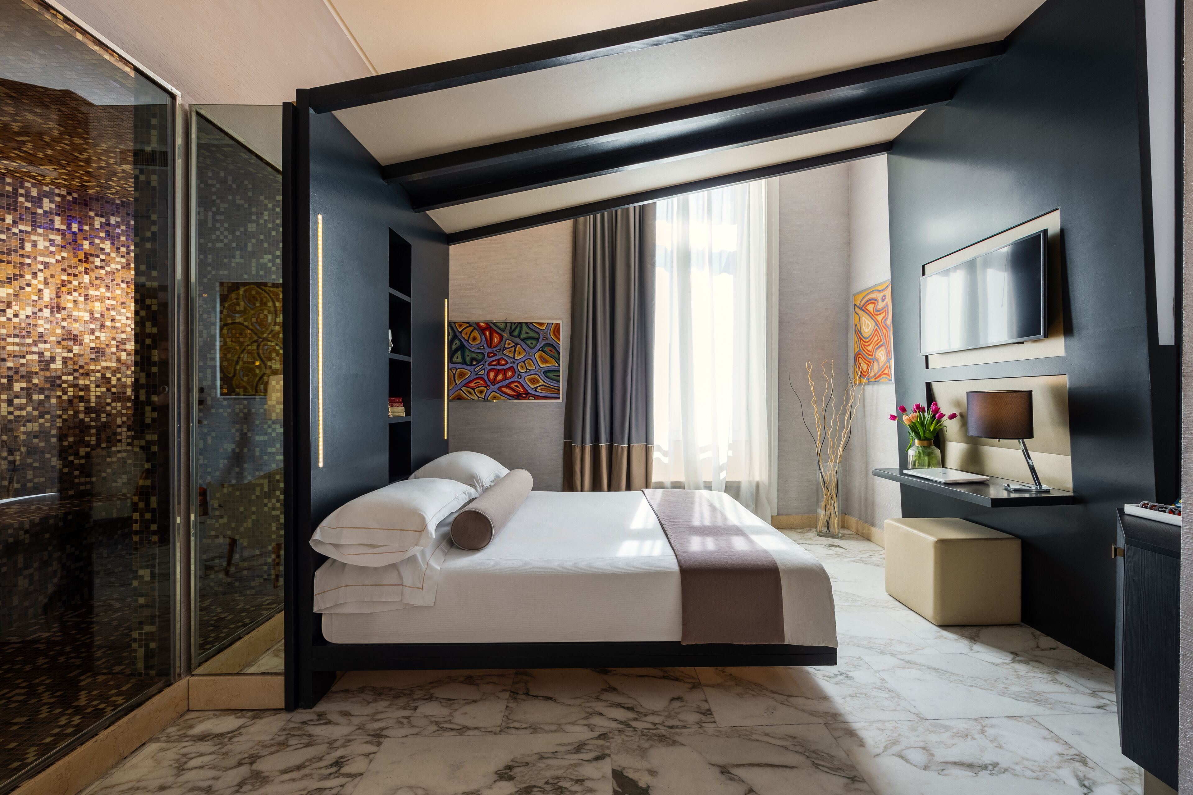 Una camera d'albergo moderna con un ampio letto, box doccia in vetro, televisione e opere d'arte alle pareti.