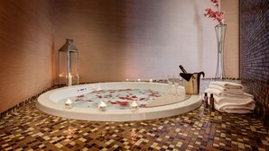 A spa room with a hot tub, candles, a vase with flowers, and towels. -  Dharma Luxury Hotel & Spa. (Rome)