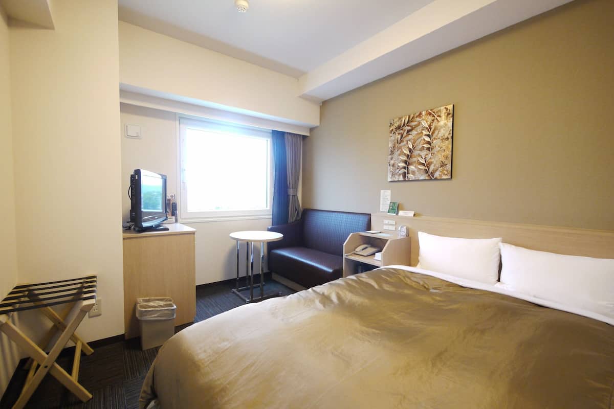 A hotel room with a large bed, a desk with a computer, a small table, and a couch.