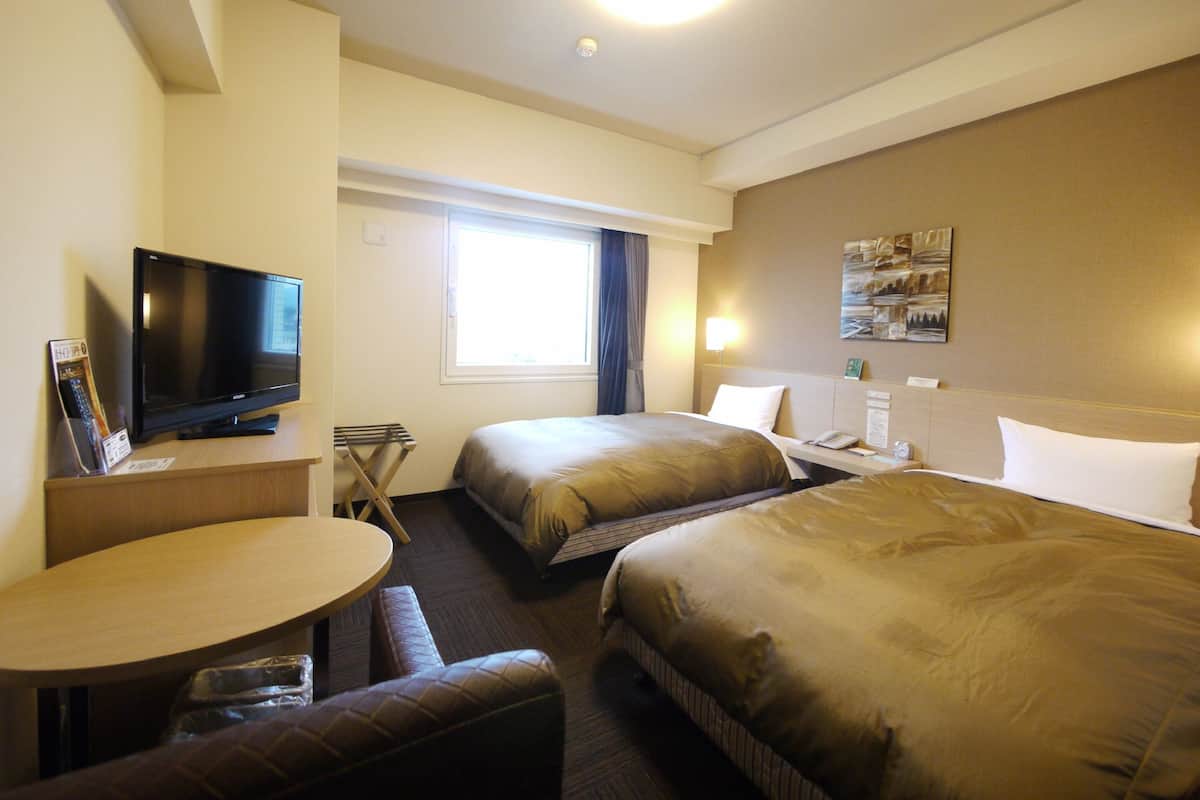 A hotel room with two beds, a TV, a desk, and a window.
