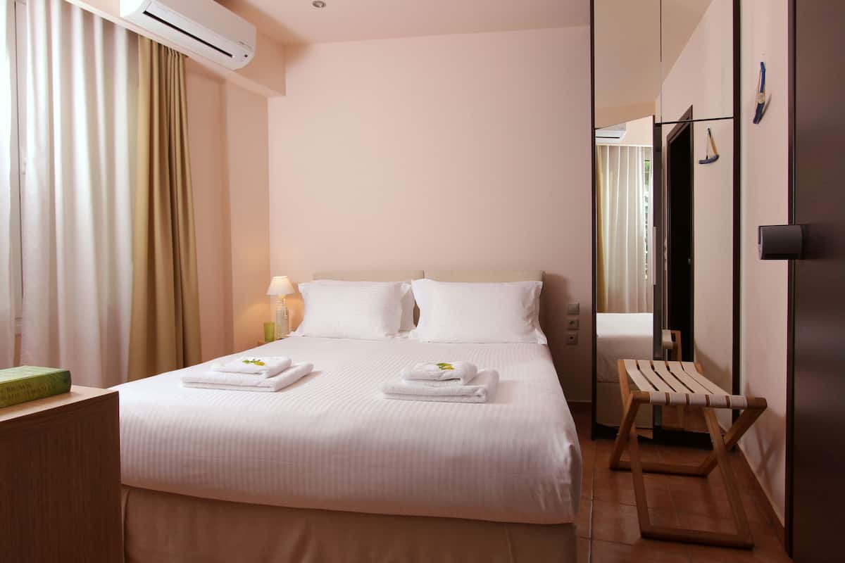 Habitación de hotel con una cama grande, dos almohadas, una mesita de noche con lámpara y una silla de madera.