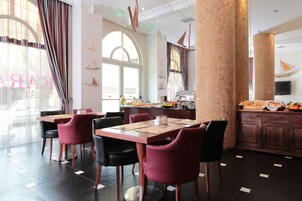 A restaurant with a breakfast bar, red and black chairs, and a buffet with fruits and pastries.