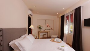 Una camera d'albergo con un letto grande, una scrivania con una lampada, un tavolino con vassoi per la colazione e un televisore appeso al muro.
