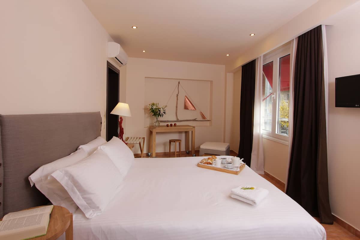 Habitación de hotel con una cama grande, un escritorio con lámpara, una mesita con una bandeja de desayuno y un televisor en la pared.