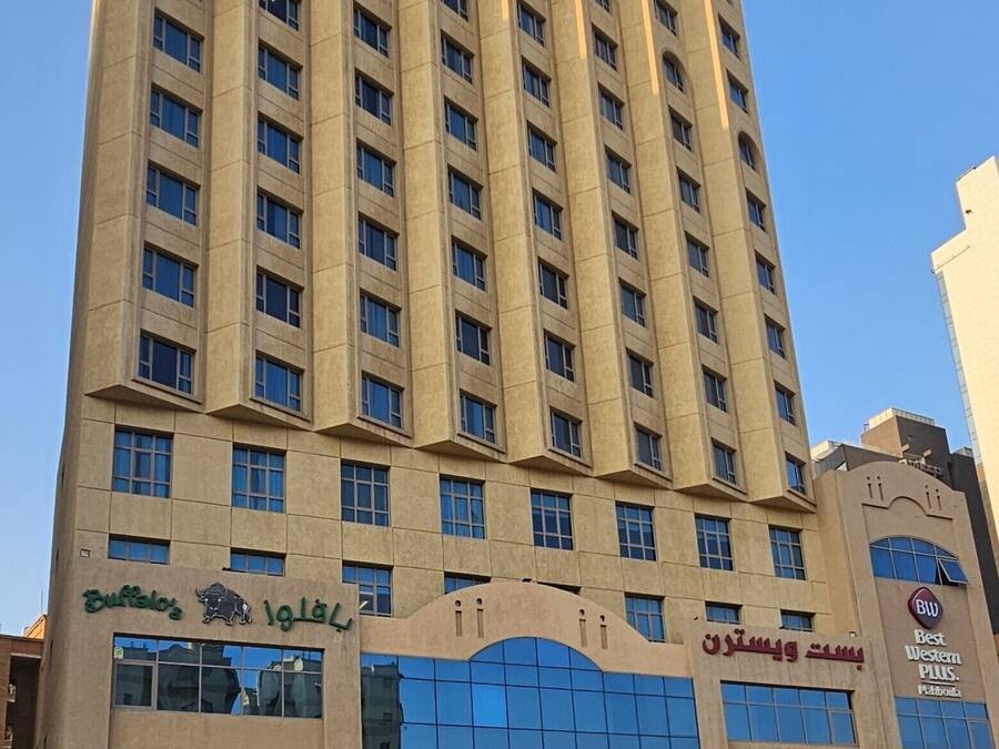 A tall hotel building with multiple floors, a glass entrance, and a sign indicating it is a Best Western Plus property.
