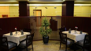 A restaurant with tables set for dining, a potted plant in the center, and wooden panel dividers.