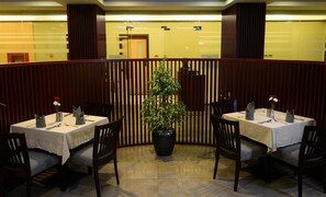A restaurant with tables set for dining, a potted plant in the center, and wooden panel dividers. - Best Western Plus Mahboula (Mahboula)