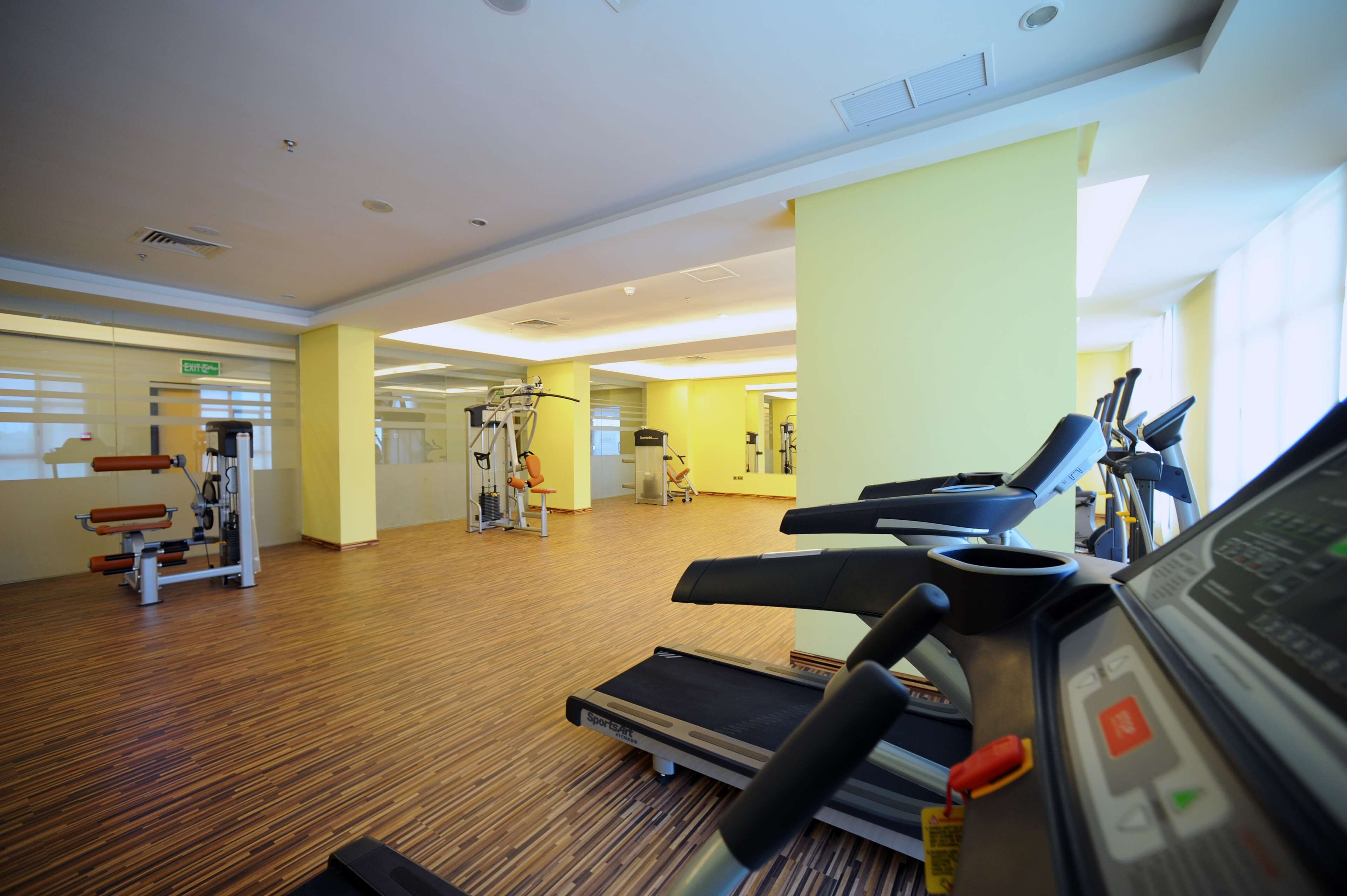 A gym with treadmills, exercise machines, and a wooden floor.