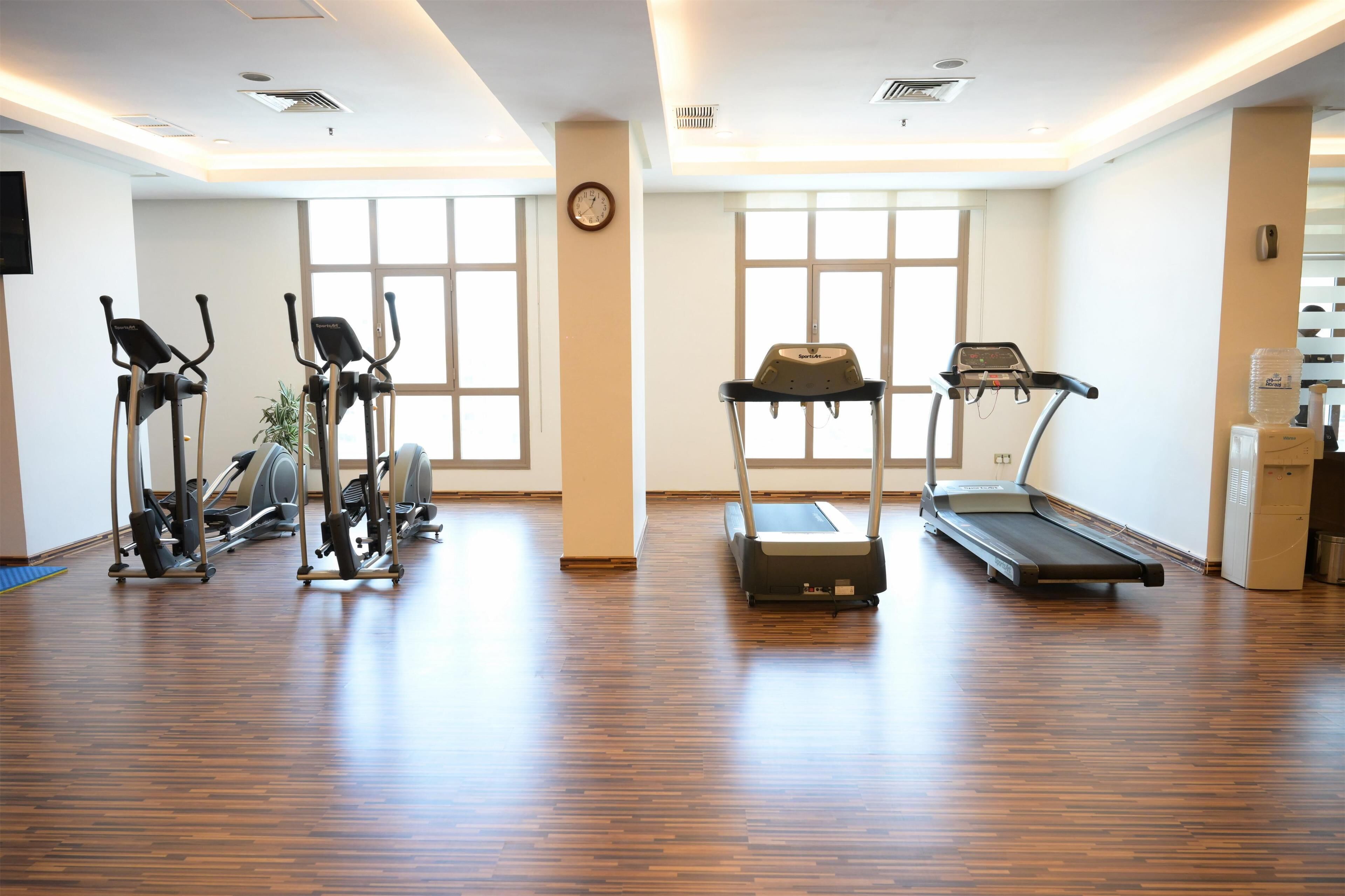 A gym with cardio equipment, large windows, and a wooden floor.