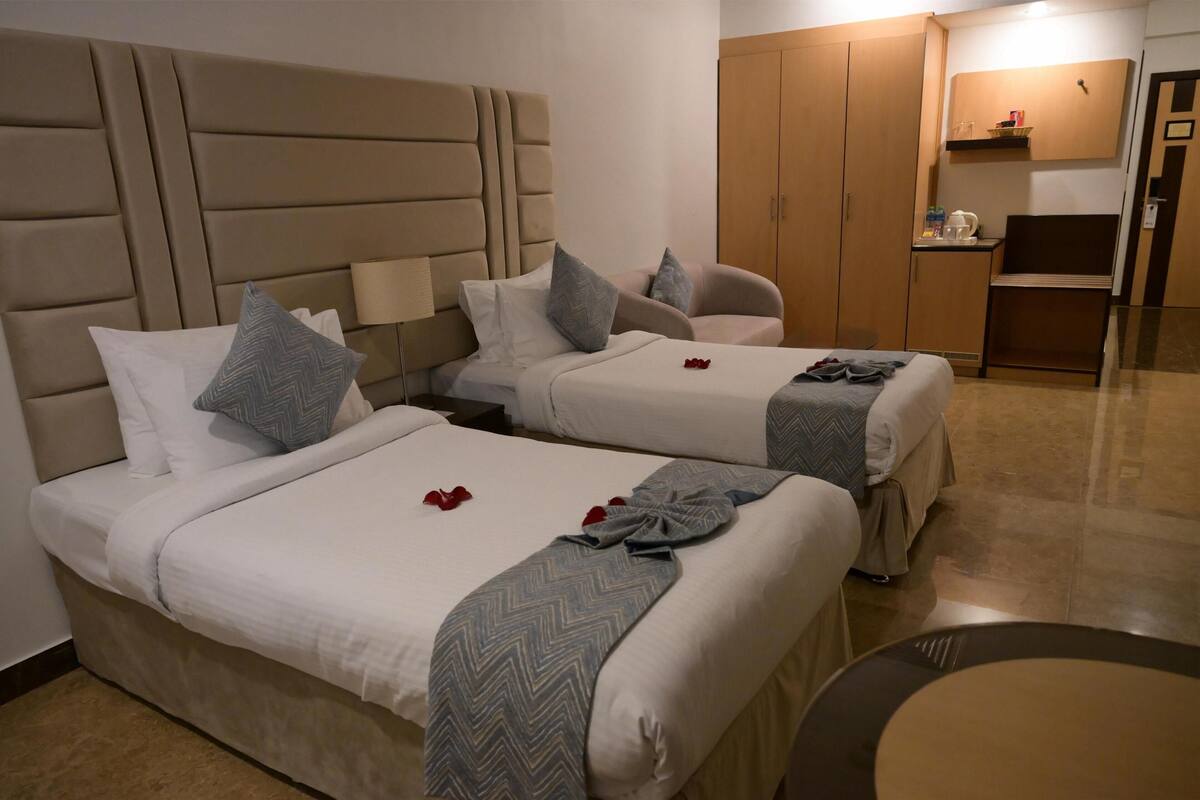 Duas camas com cabeceiras, uma mesinha e um guarda-roupa num quarto de hotel.