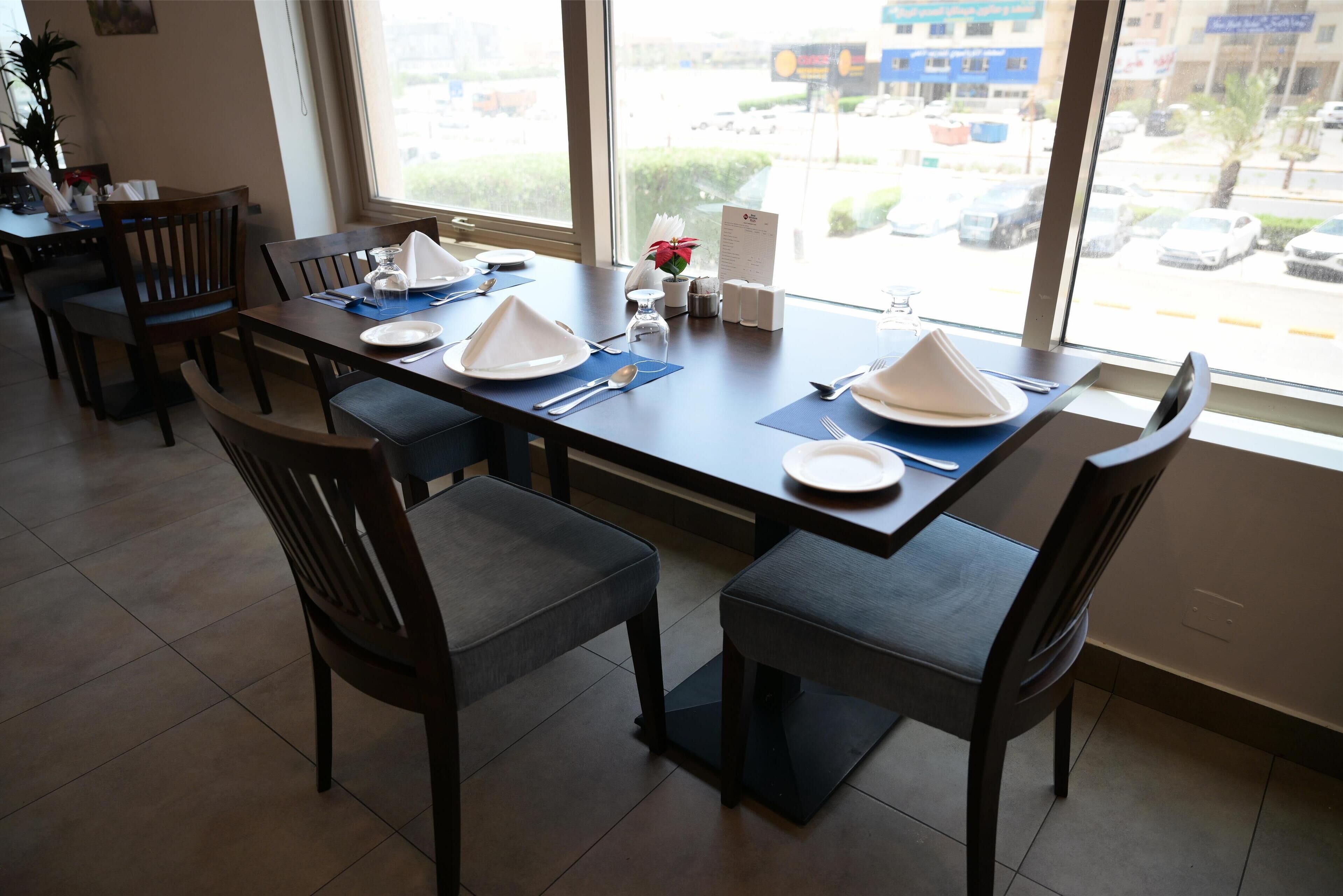 A dining area with a table set for four, chairs, and a view of the street through large windows.