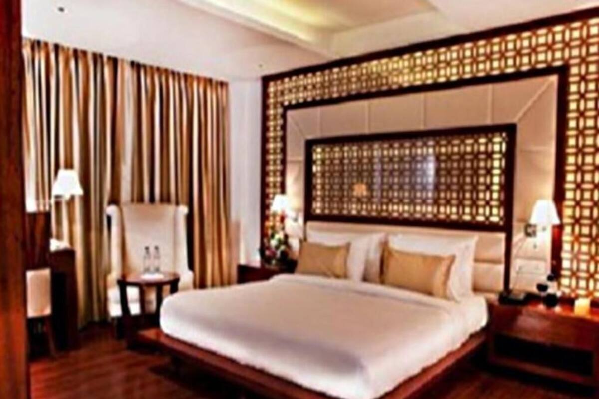 A hotel room with a large bed, wooden headboard, nightstands, and a lamp.