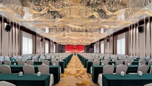 Una sala conferenze con file di tavoli e sedie, una moquette decorata e uno striscione rosso sullo sfondo.