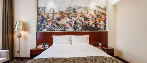 A hotel room with a large bed, a headboard with artwork, a bedside table with a lamp, and a chair.