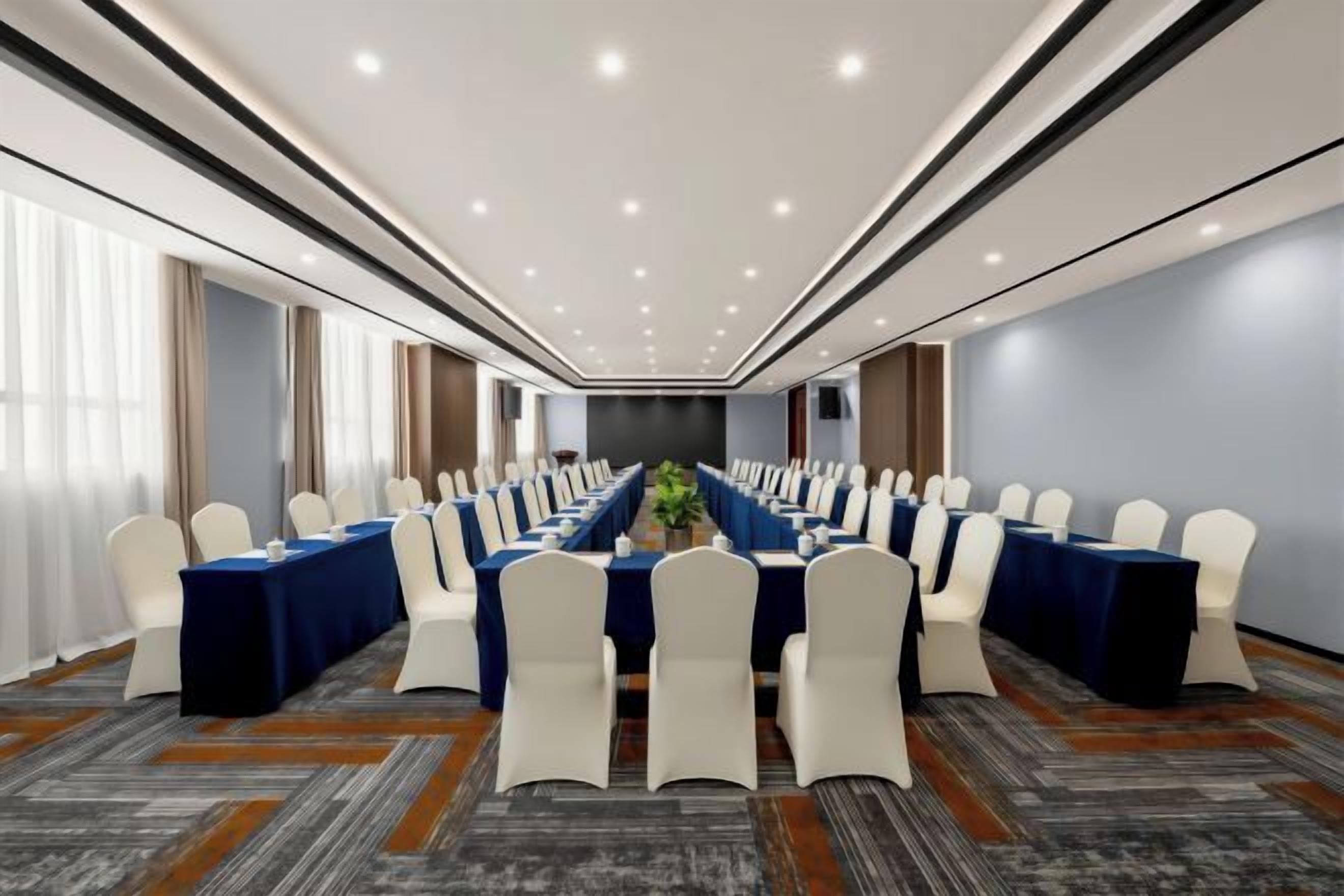 Une salle de conférence avec une longue table, des chaises blanches et un sol recouvert de moquette.
