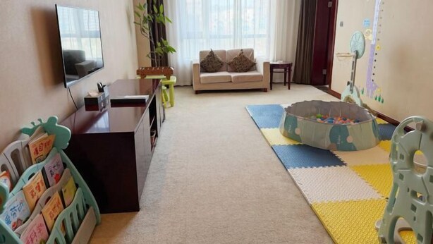 A living room with a sofa, TV, bookshelf, and a play area with a ball pit. - Intercity Hotel (Baoji)