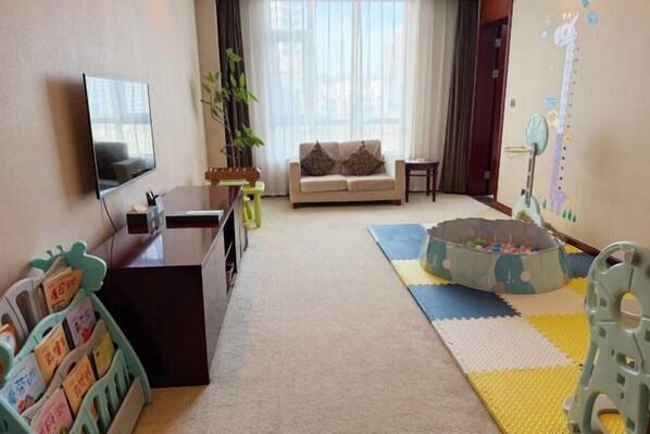 Una sala de estar con sofá, televisor, estantería y una zona de juegos con piscina de pelotas.