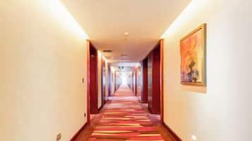 A hotel corridor with a carpeted floor, wooden doors, and a painting on the wall.