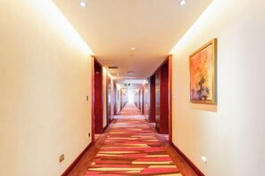 A hotel corridor with a carpeted floor, wooden doors, and a painting on the wall. - Intercity Hotel (Baoji)