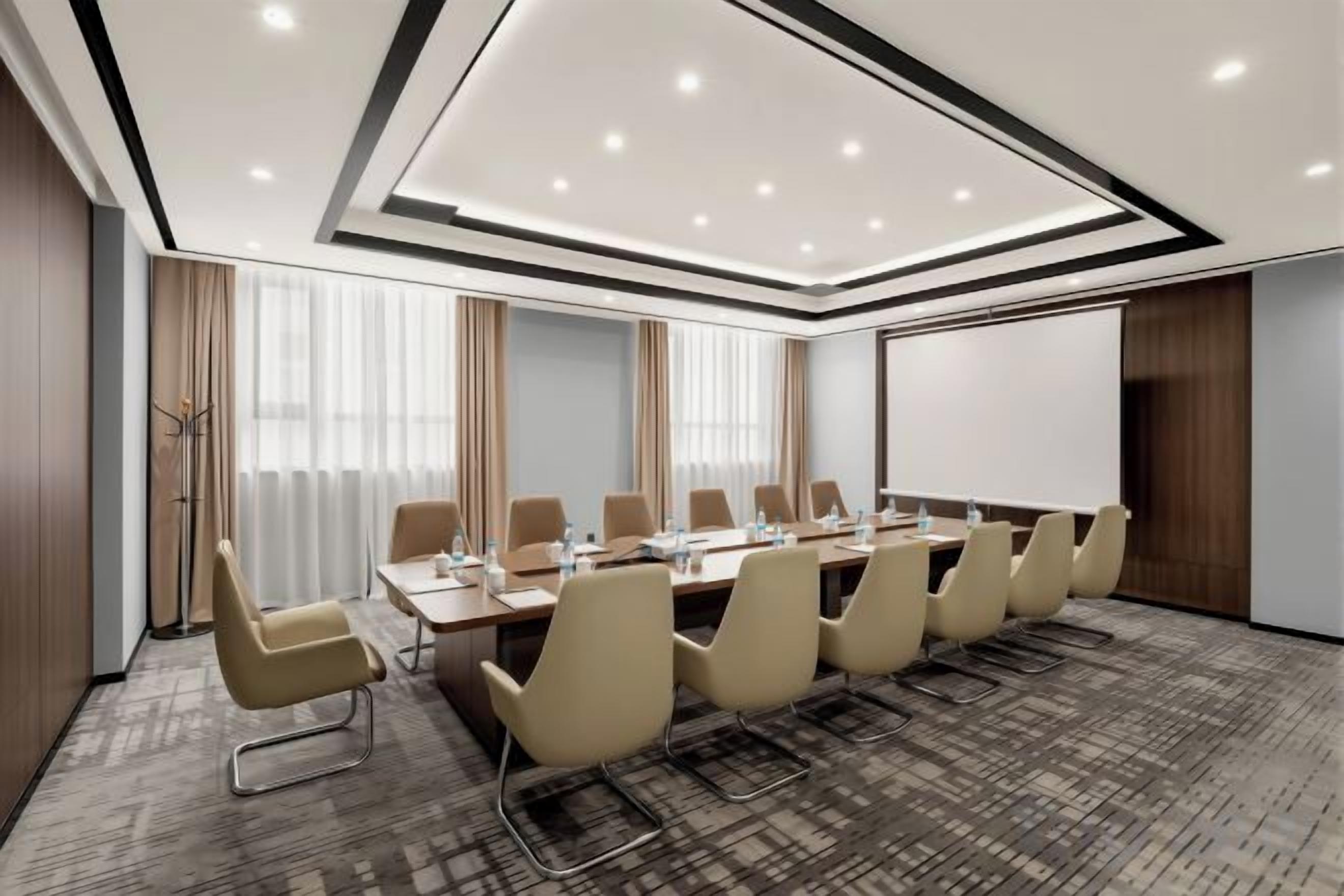 A conference room with a long table, chairs, a projector screen, and a carpeted floor.