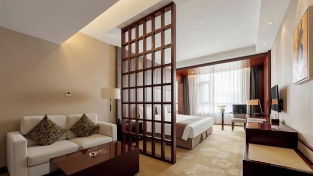 A hotel room with a sofa, a coffee table, a bed, a TV, and a decorative screen. - Intercity Hotel (Baoji)