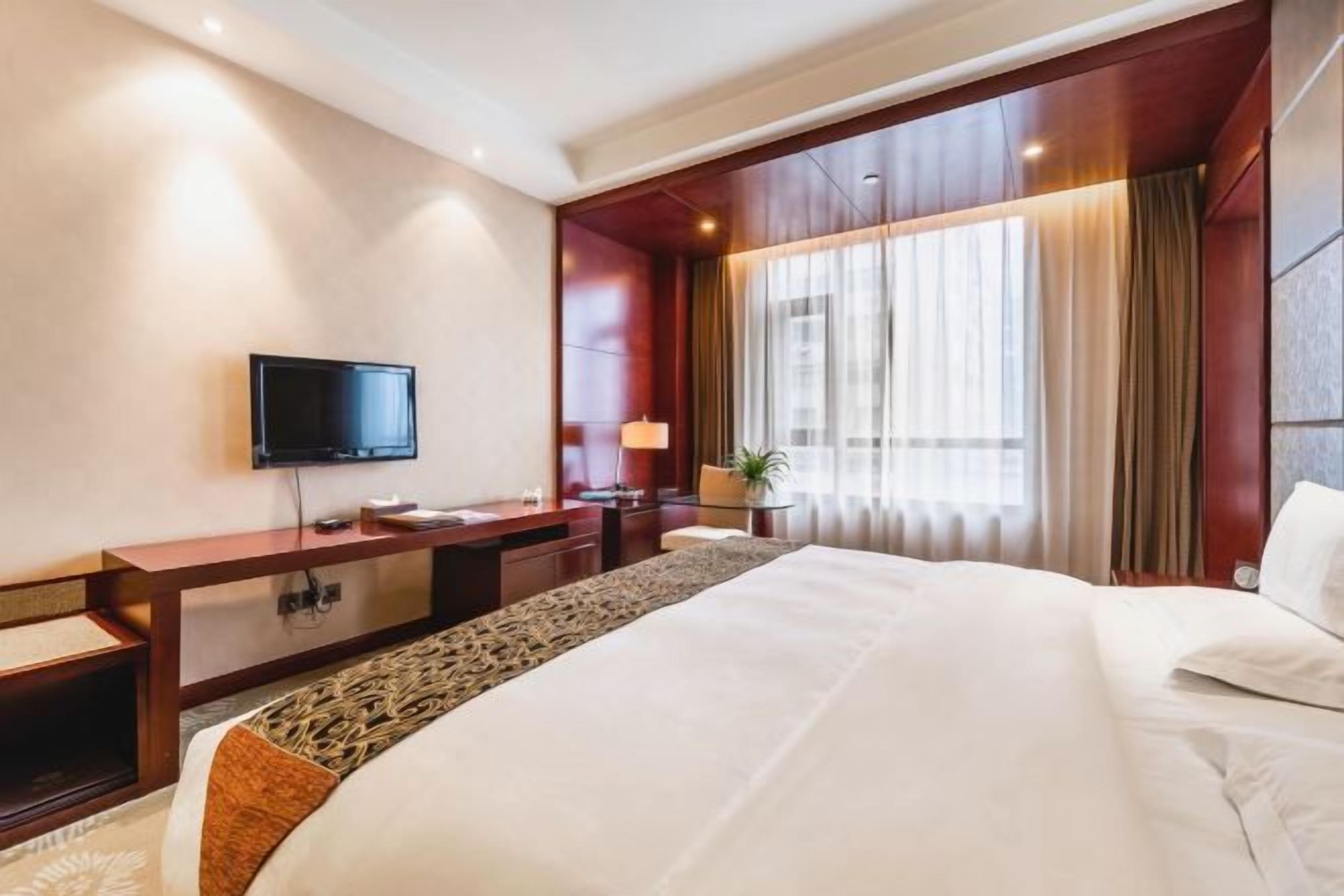 A hotel room with a large bed, a flat-screen TV, a desk, and a window with curtains.