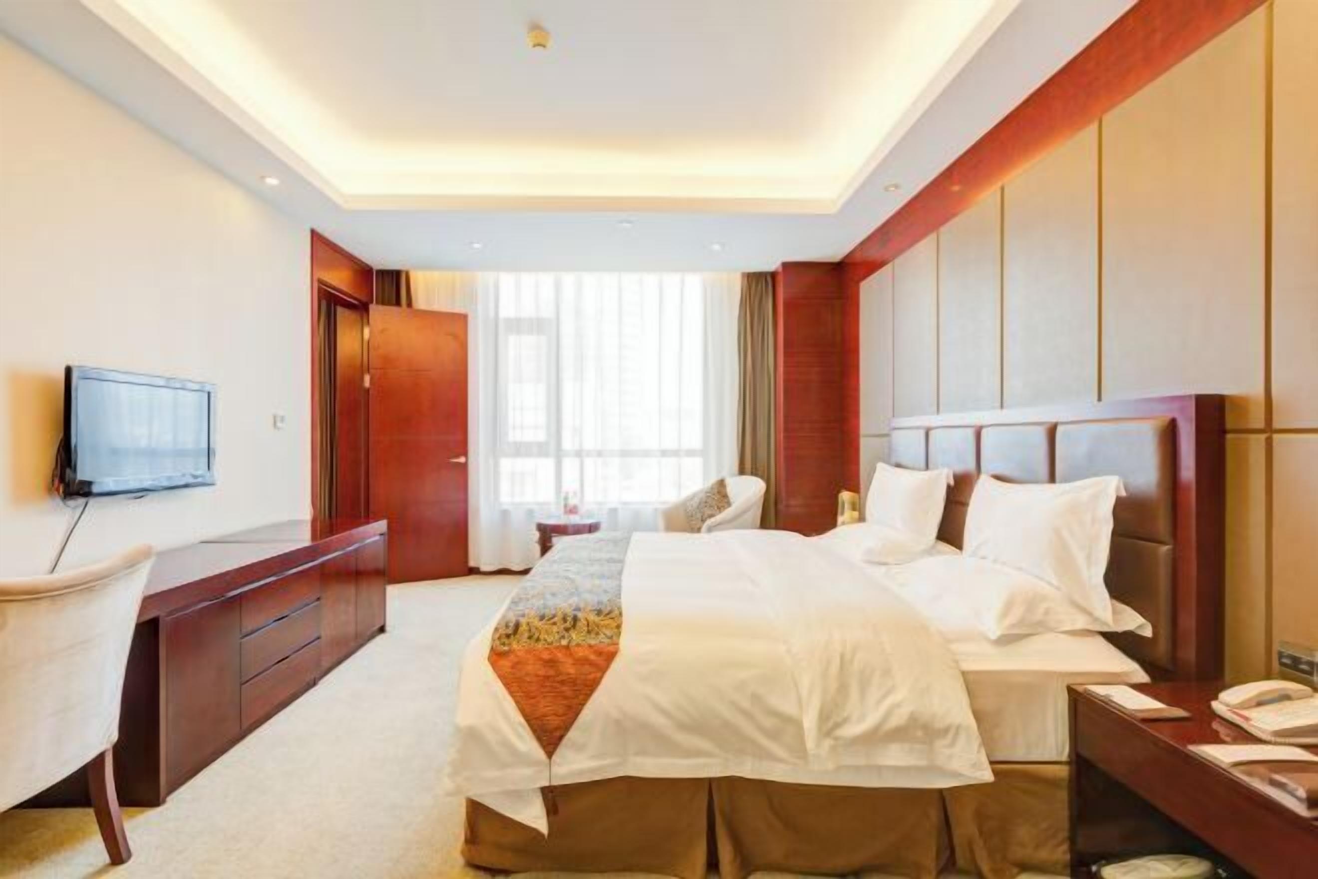 Una habitación de hotel con cama, escritorio, silla, televisor y ventana con cortinas.