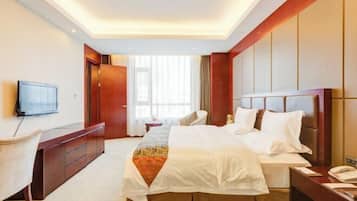 Una camera d'albergo con un letto, una scrivania, una sedia, una televisione e una finestra con tende.