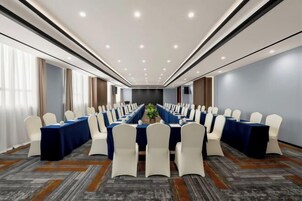 Un salón de conferencias con una larga mesa, sillas blancas y un mantel azul.