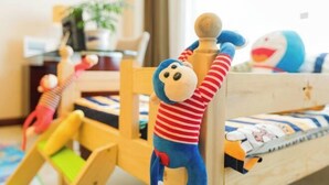 A child's bed with a wooden headboard, a plush toy hanging on it, and a colorful play mat on the floor. - Intercity Hotel (Baoji)