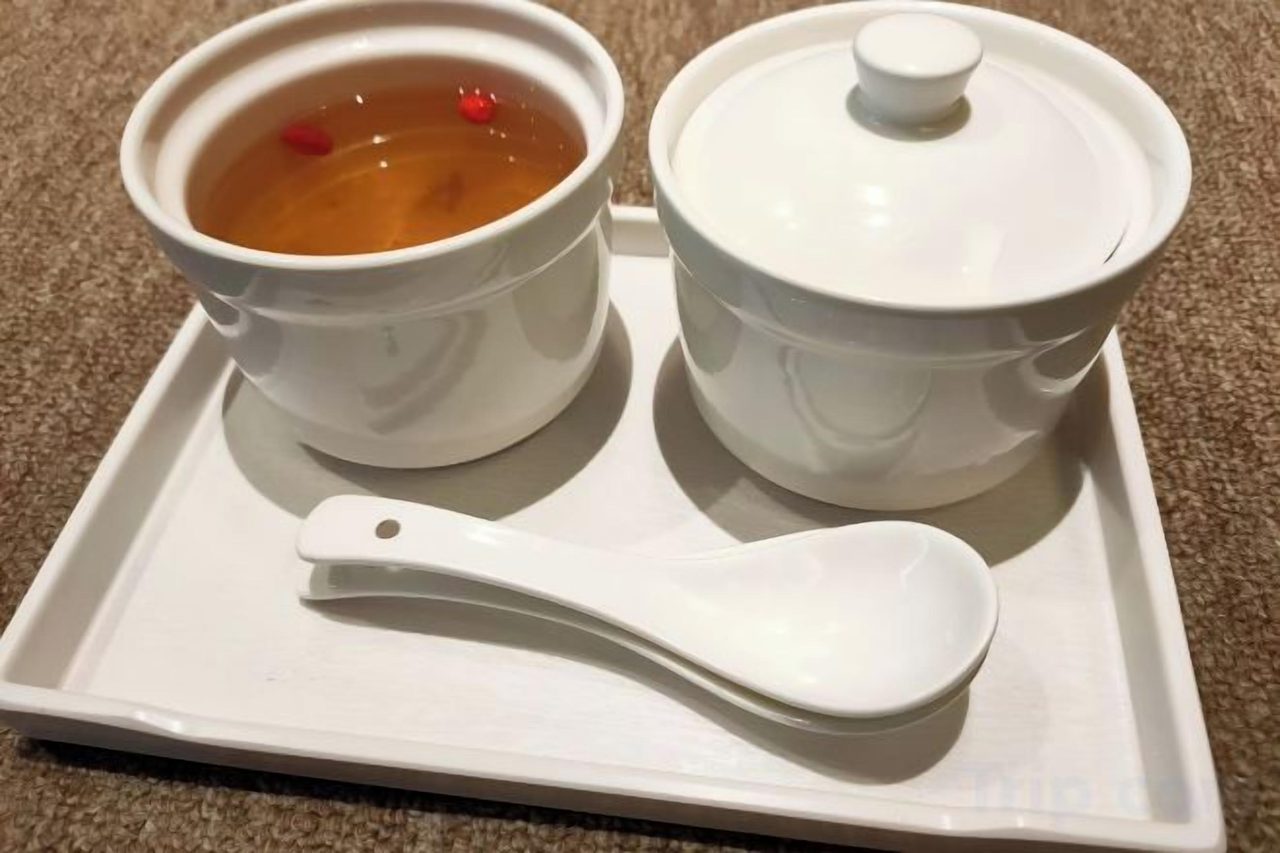 A tray with two white ceramic bowls, one with a lid and one without, and a white spoon.
