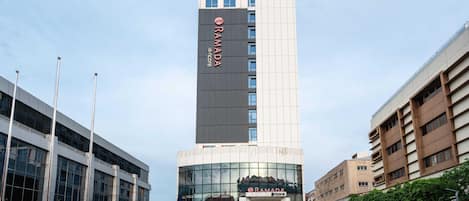 A modern hotel building with a prominent logo, a glass facade, and a parking area.