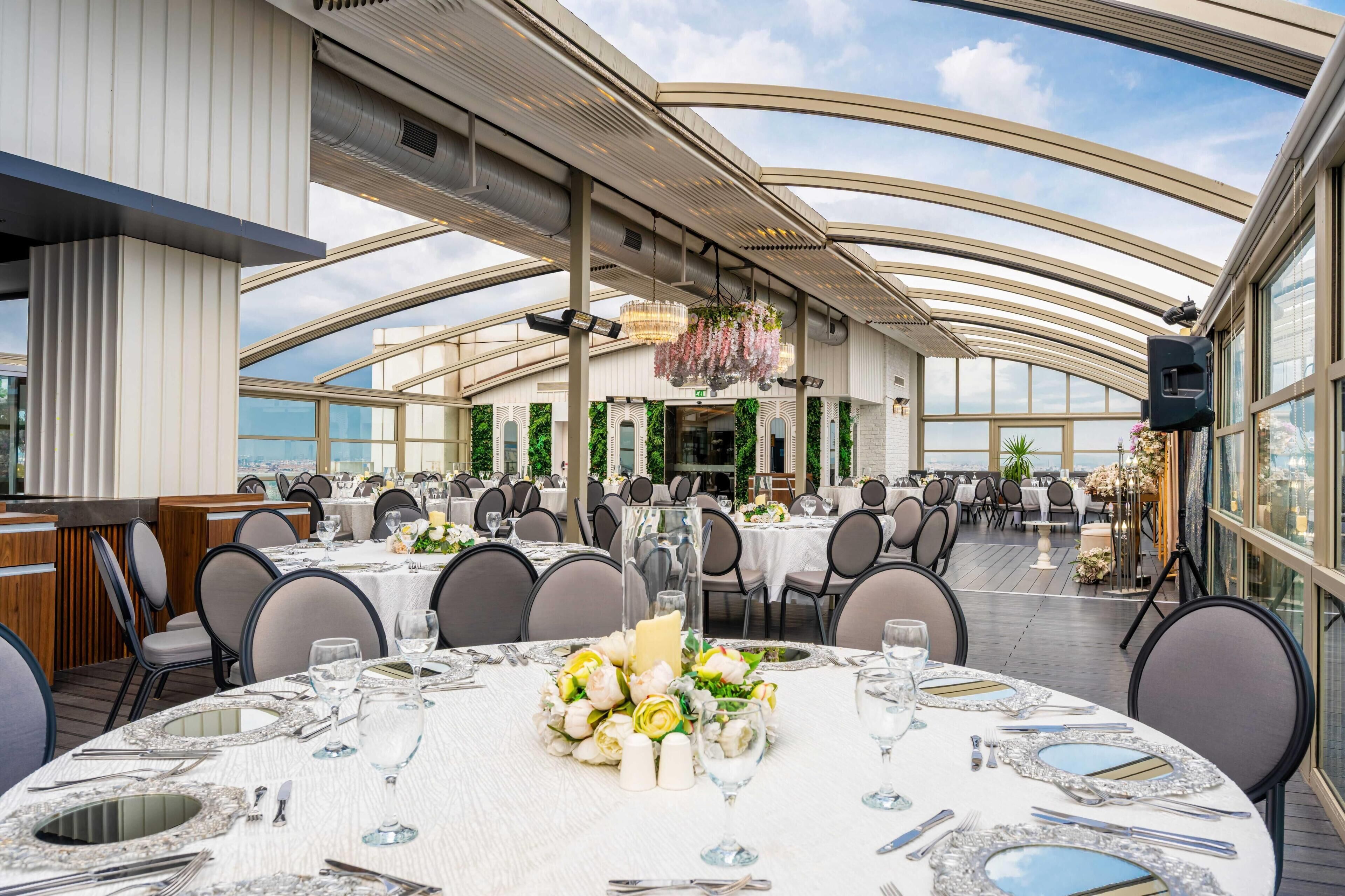 A spacious dining area with round tables set for a meal, featuring a view of the city through large windows.