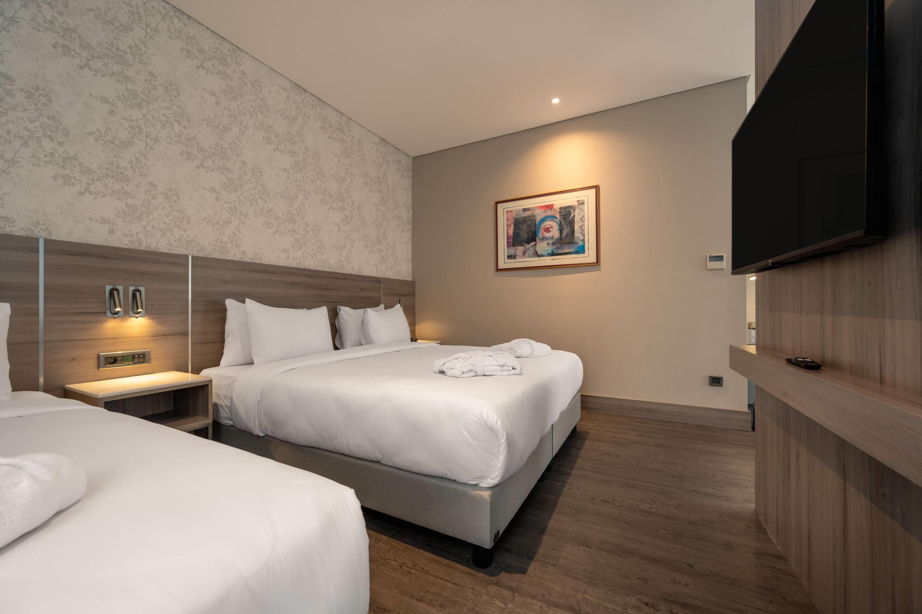 A hotel room with two beds, a flat-screen TV, a painting on the wall, and a wooden floor.