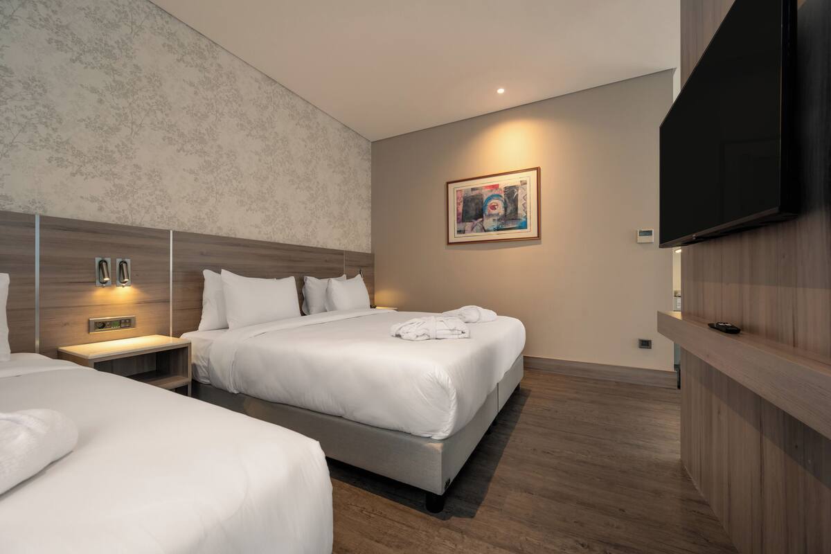 Una habitación de hotel moderna con dos camas, un televisor de pantalla plana, un cuadro en la pared y una cabecera de madera.