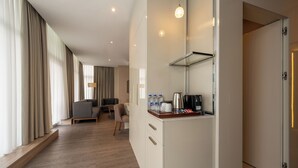 A modern hotel room with a wooden floor, a kitchenette with a coffee maker, and a seating area with a sofa and chairs. - Ramada Encore by Wyndham Istanbul Bayrampasa (Istanbul)