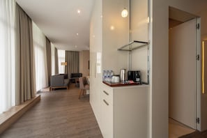 Ein modernes Hotelzimmer mit Holzboden, einer Küchenzeile mit Kaffeemaschine und einer Sitzecke mit Sofa und Sesseln.