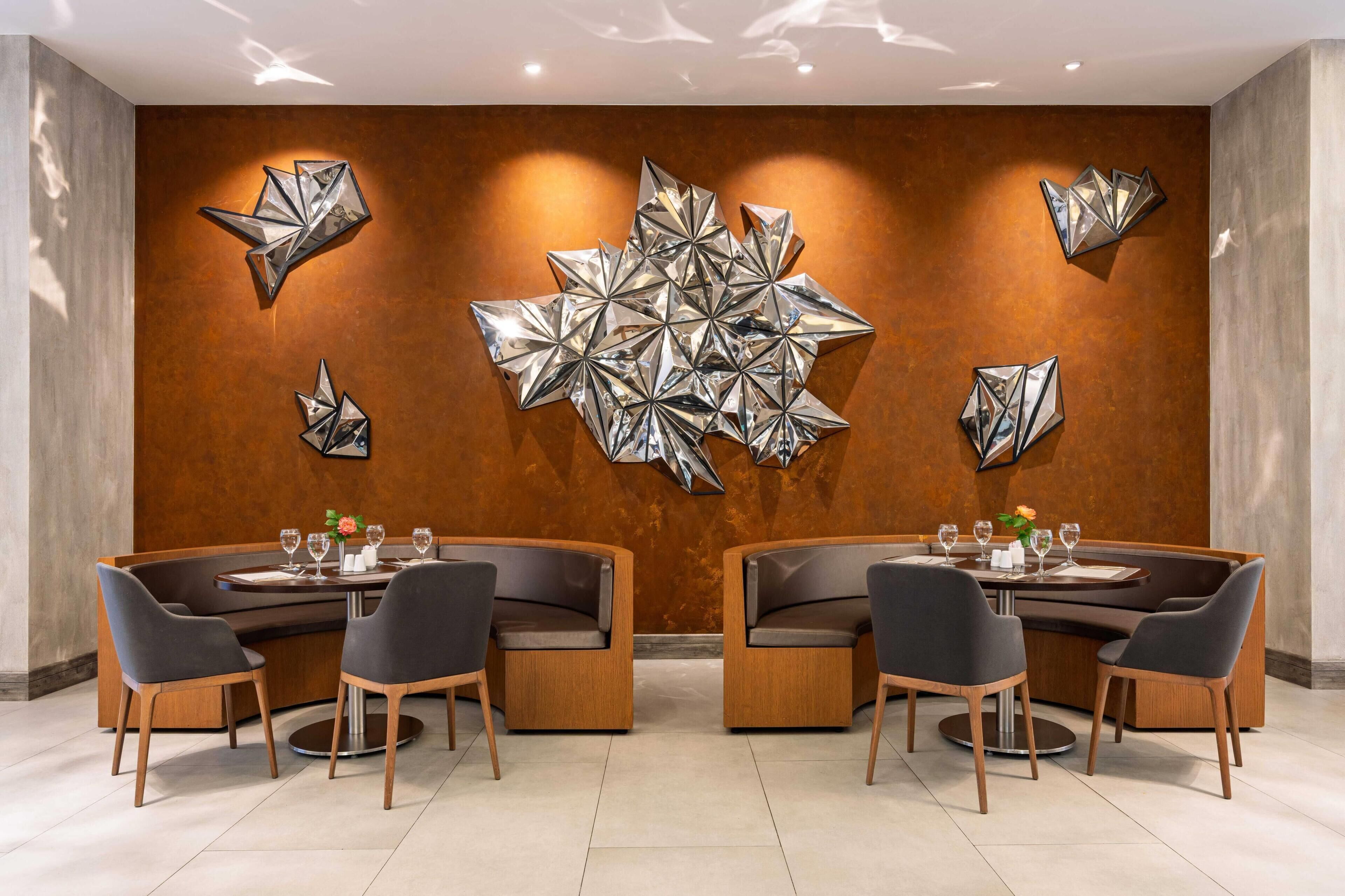 A modern dining area with a central table surrounded by booths, a decorative wall with geometric metal art, and a warm-toned wall.