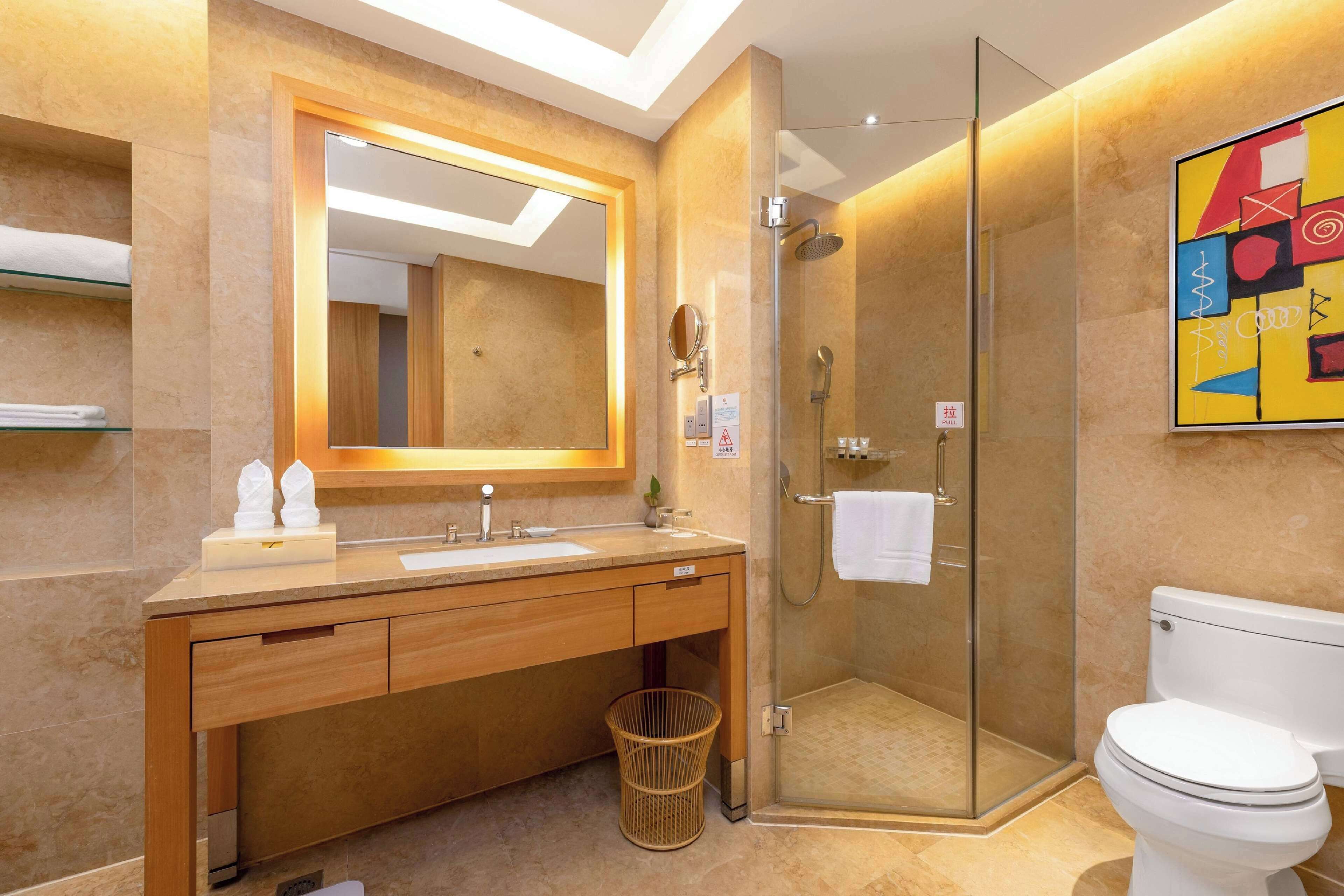 A modern bathroom with a glass-enclosed shower, a wooden vanity with a mirror, and a white toilet.