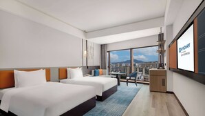 Une chambre d’hôtel avec deux lits, un bureau et une grande fenêtre donnant sur la ville.