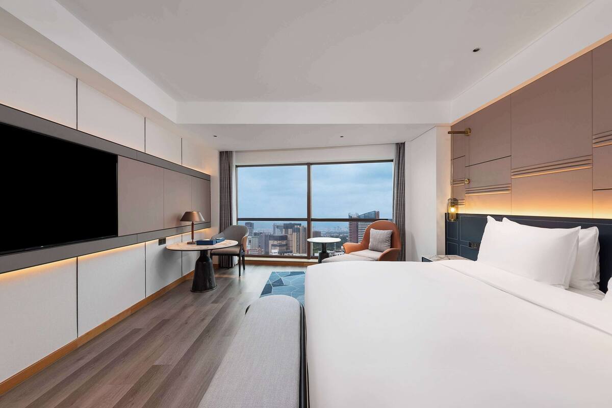 Habitación de hotel moderna con una cama grande, un televisor de pantalla plana, un escritorio y vistas del horizonte de la ciudad.